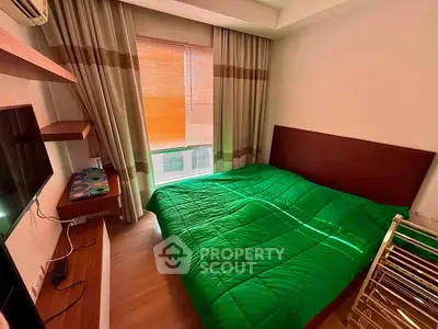 Cozy bedroom with green bedding and natural light from window, ideal for relaxation.
