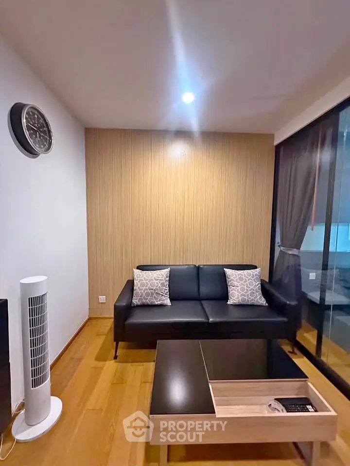 Modern living room with sleek black sofa, wooden flooring, and stylish decor in a cozy apartment.