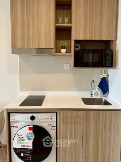 Modern kitchen with wooden cabinets and built-in appliances, featuring a washing machine and microwave.