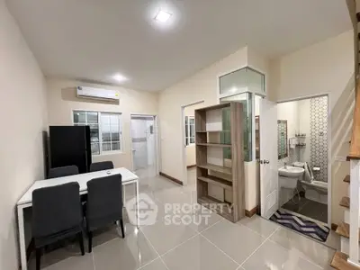 Modern open-plan living area with dining set and adjacent bathroom, featuring sleek tile flooring.