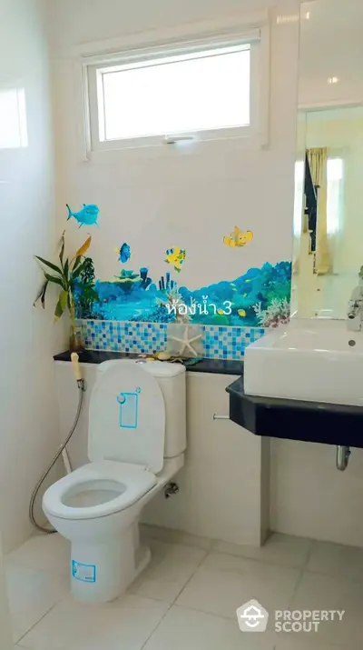 Bright and playful bathroom with aquatic-themed wall tiles, modern fixtures, and ample natural light from a high window.