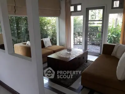 Cozy living room with large windows and garden view, featuring modern furniture and natural light.