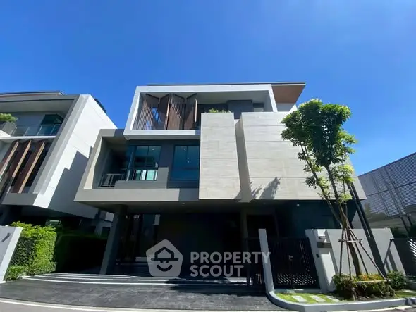 Modern three-story house with sleek design and large windows under clear blue sky.