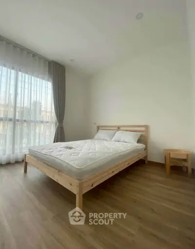 Spacious bedroom with wooden flooring and large window for natural light.