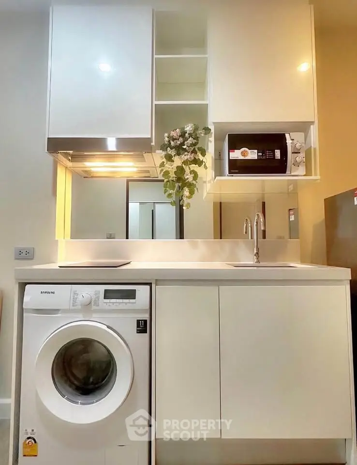 Modern compact kitchen with washing machine and microwave, sleek cabinetry, and elegant lighting.