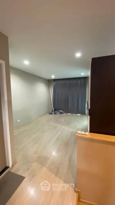 Spacious empty room with wooden flooring and large window, ideal for customization.