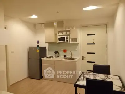 Modern kitchen with sleek cabinetry, stainless steel fridge, and dining area in a cozy apartment.