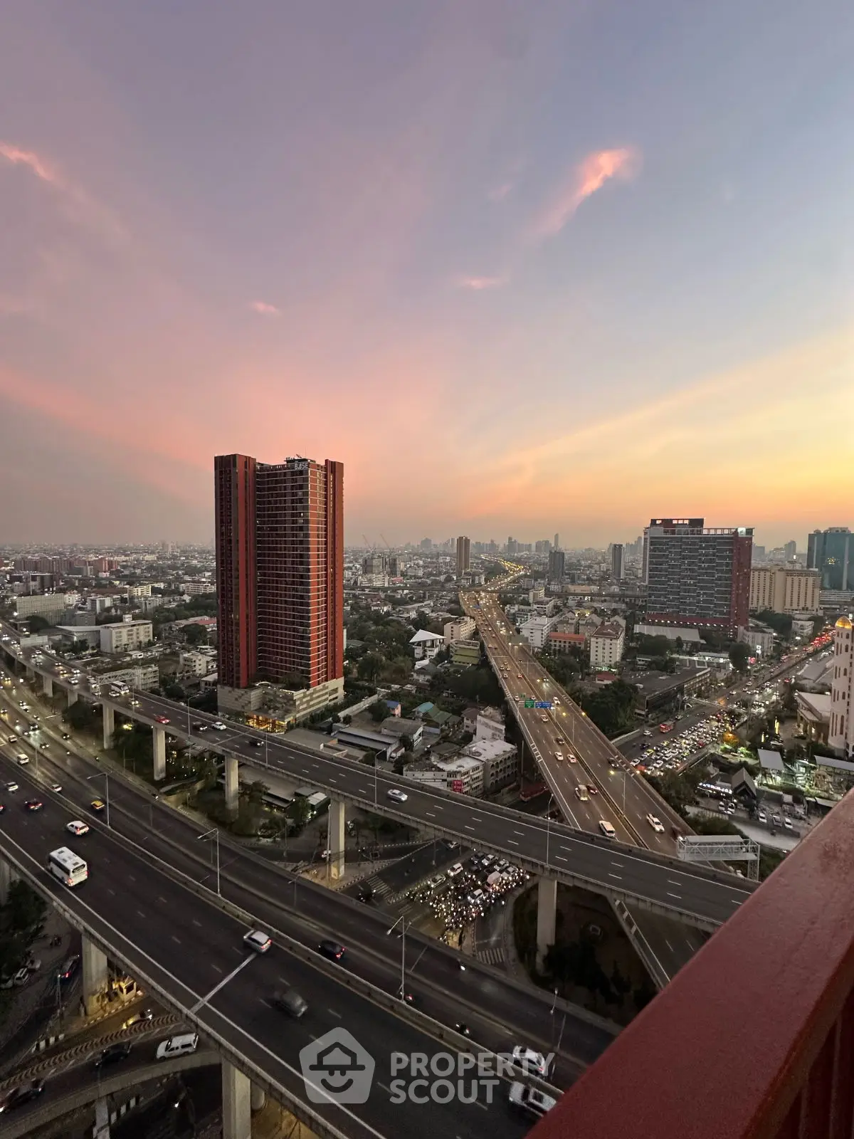 Stunning cityscape view from high-rise balcony at sunset, showcasing vibrant urban skyline and bustling highways.