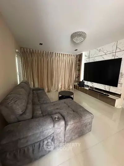 Luxurious living room with plush gray sofa and large TV, perfect for entertainment.