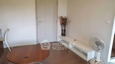 Cozy living room with wooden flooring and minimalist decor, featuring a round table and decorative vase.