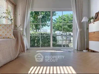 Bright living room with large windows and garden view, featuring modern decor and natural light.