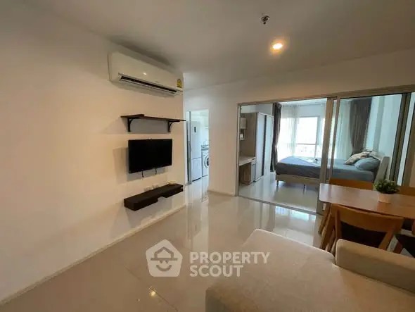 Modern apartment interior with open living room and bedroom view, featuring sleek furniture and bright lighting.