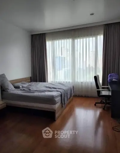 Spacious bedroom with large window and city view, featuring a comfortable bed and study desk.