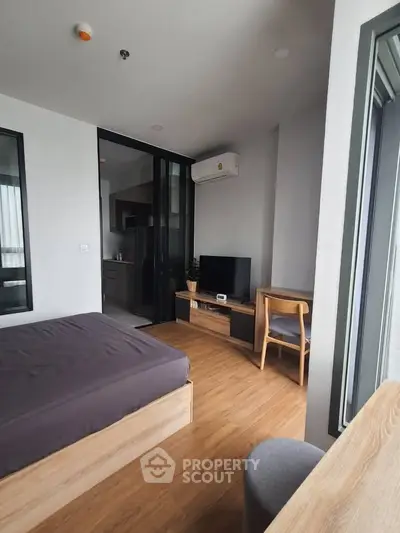 Modern studio apartment with wooden flooring, cozy bed, and sleek kitchen area.