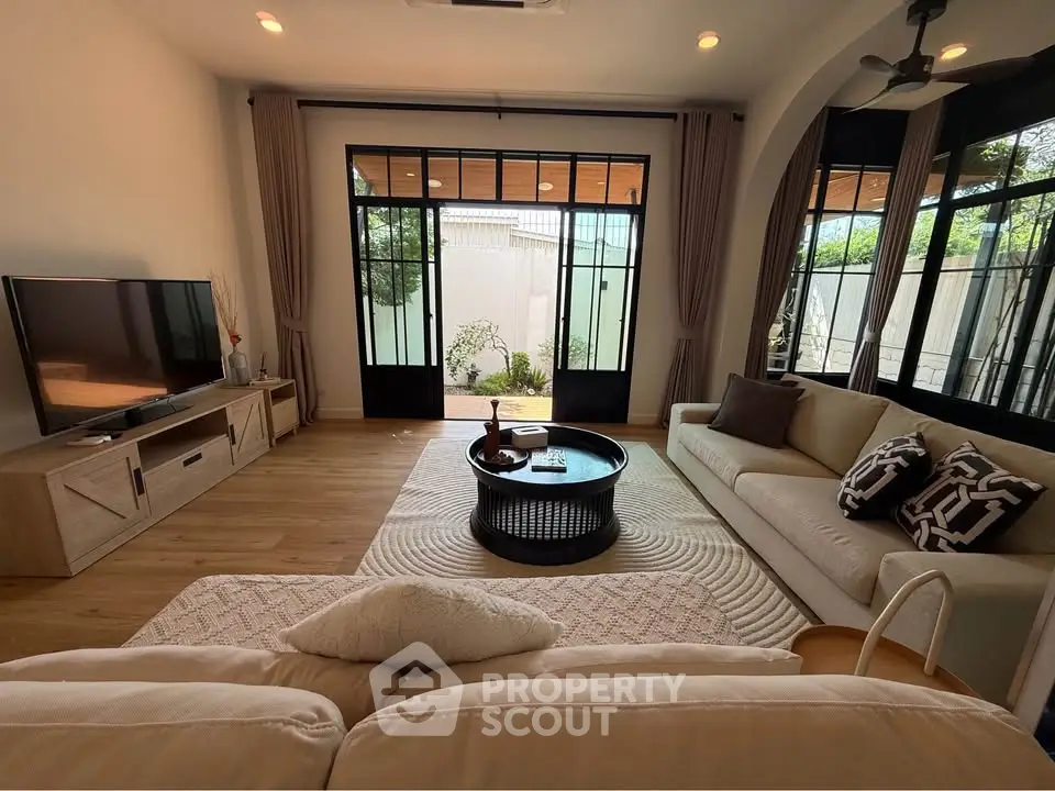 Spacious living room with elegant decor and garden view, featuring large windows and cozy seating area.