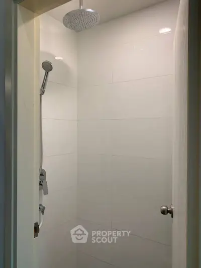Modern minimalist shower with sleek white tiles and rainfall showerhead in a compact bathroom.