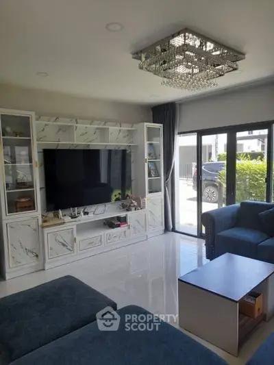 Elegant living room with modern chandelier and large TV, featuring stylish marble cabinetry and plush blue seating.