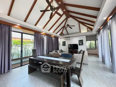 Spacious living room with vaulted ceiling and elegant wooden beams, featuring modern furniture and large windows.