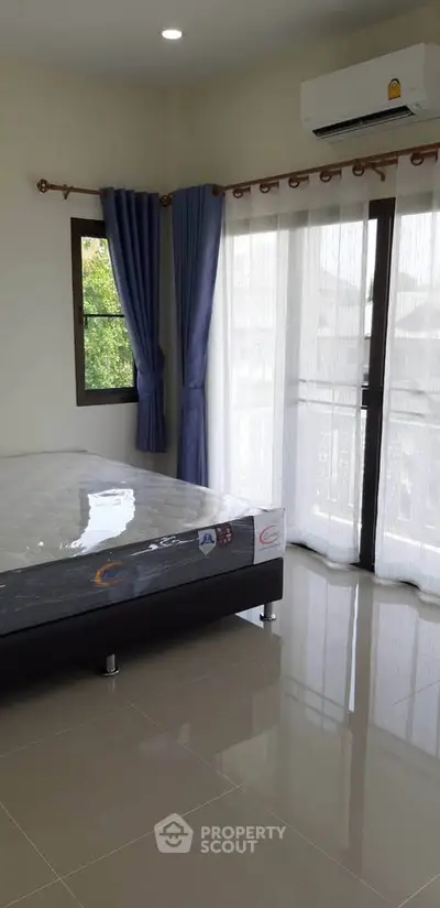 Spacious bedroom with large windows and natural light, featuring a comfortable bed and modern air conditioning.