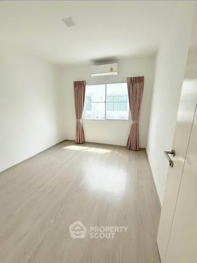 Bright empty bedroom with wooden flooring and air conditioning, ready for customization.