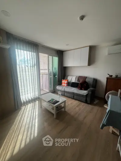 Cozy living room with natural light, modern sofa, and sliding glass doors leading to a balcony.
