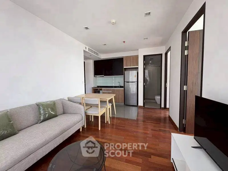 Modern open-plan living room with kitchen and dining area, featuring sleek furniture and wooden flooring.