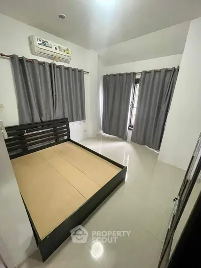 Spacious and well-lit bedroom with a large window, modern air conditioning unit, and elegant dark curtains complementing the minimalist decor.