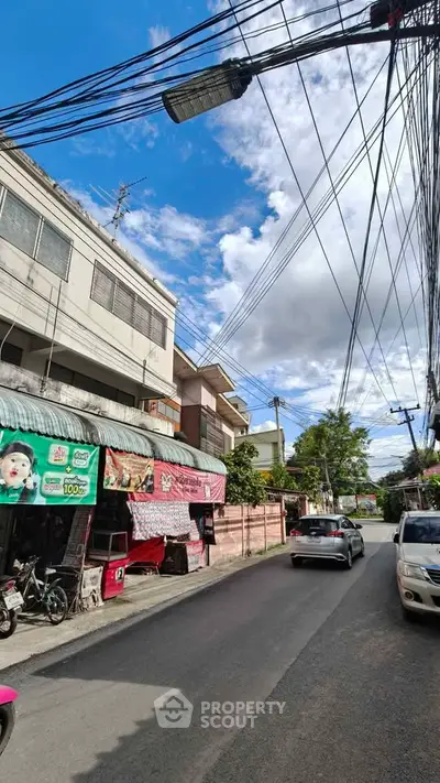 Street view of residential area with buildings and parked cars under a clear blue sky.