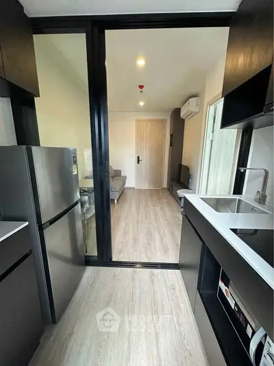 Modern kitchen with sleek black cabinetry and open layout leading to living area.