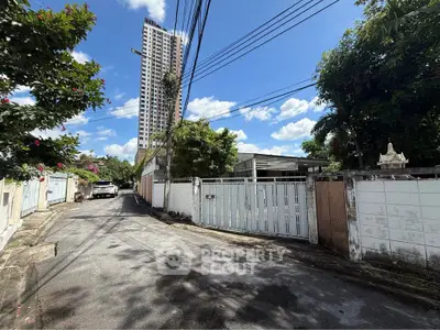 Charming residential street with towering high-rise and lush greenery under clear blue sky.