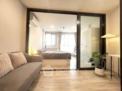 Modern bedroom with glass partition and cozy living area, featuring stylish decor and natural light.