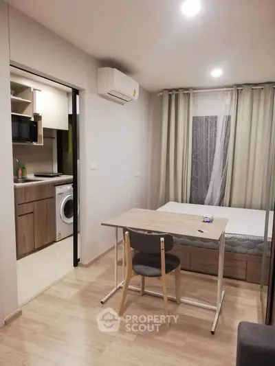 Modern studio apartment with compact kitchen and cozy living area, featuring a washing machine and air conditioning.