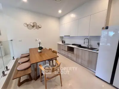 Modern kitchen with sleek cabinetry and dining area, featuring a minimalist design and open layout.