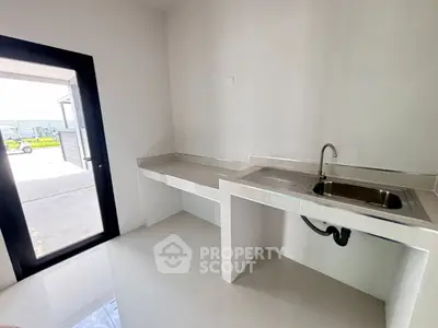 Modern minimalist kitchen with sleek countertops and stainless steel sink, bright natural lighting.