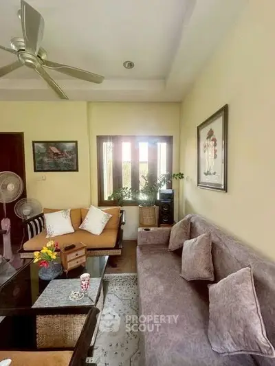 Cozy living room with plush sofa, ceiling fan, and natural light from large window.