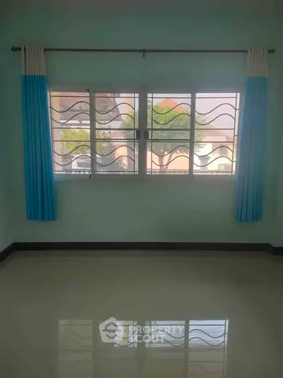 Spacious room with large window and blue curtains, perfect for natural light and airy ambiance.
