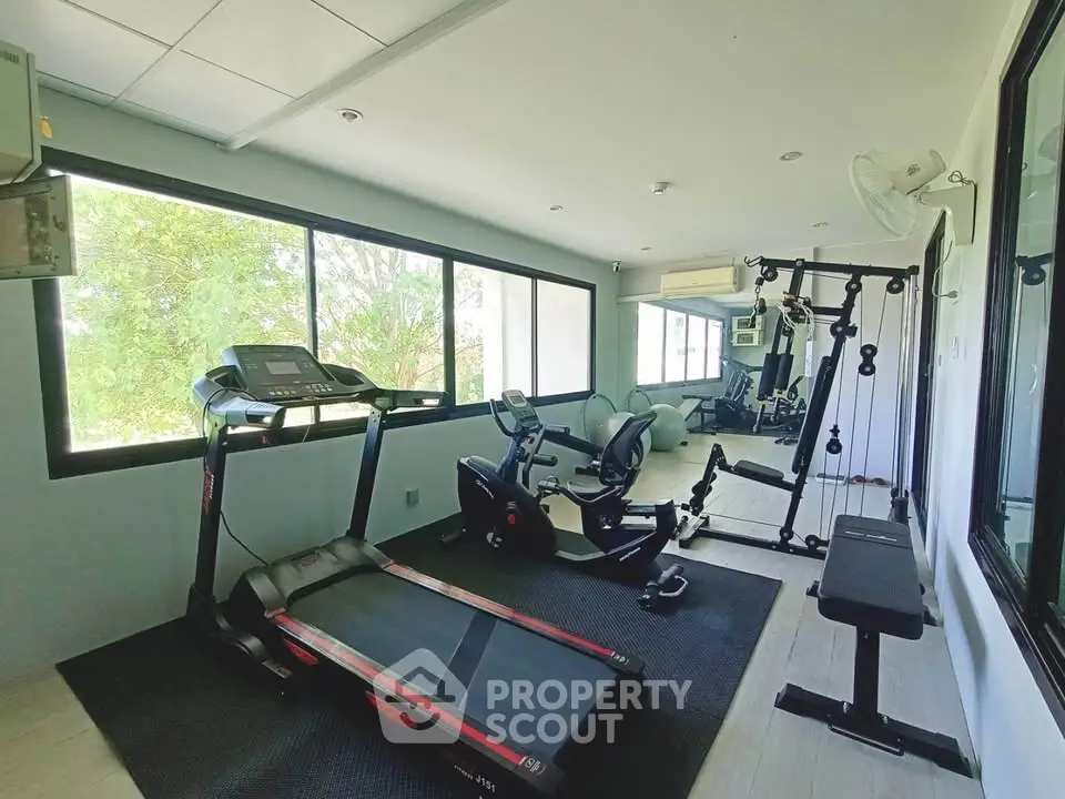 Modern gym with exercise equipment and large windows in a real estate property.