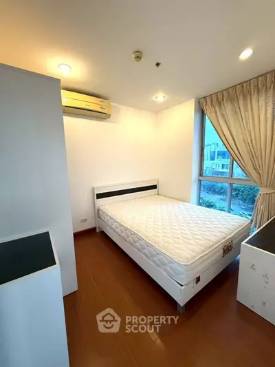 Bright bedroom with large window and modern furnishings in a high-rise apartment.