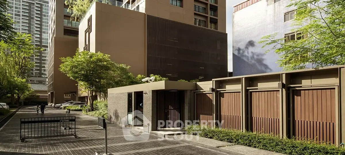 Modern building entrance with sleek design and lush greenery in urban setting.