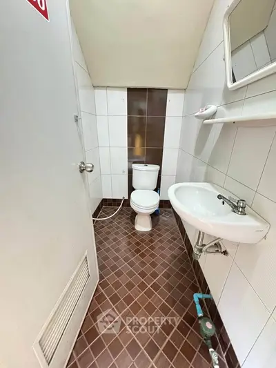 Compact bathroom with white fixtures and brown tiled floor, featuring a toilet and sink.