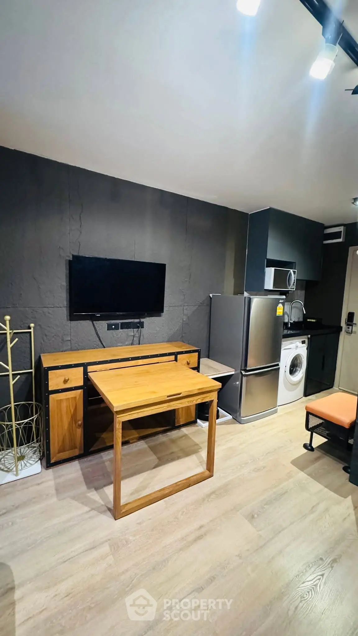 Modern studio apartment with sleek kitchen and cozy living area, featuring a washing machine and fridge.