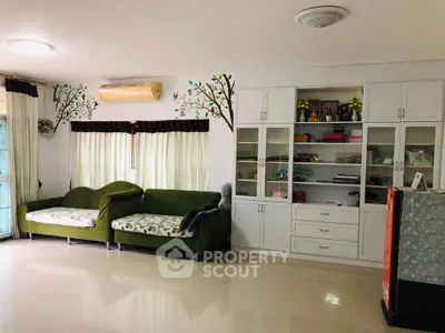 Spacious living room with modern decor and ample natural light, featuring stylish green sofas and built-in cabinets.