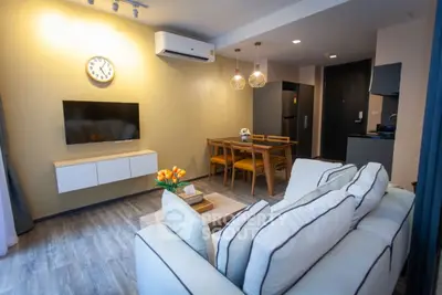 Modern living room with stylish furniture and open dining area, featuring a wall-mounted TV and air conditioning.
