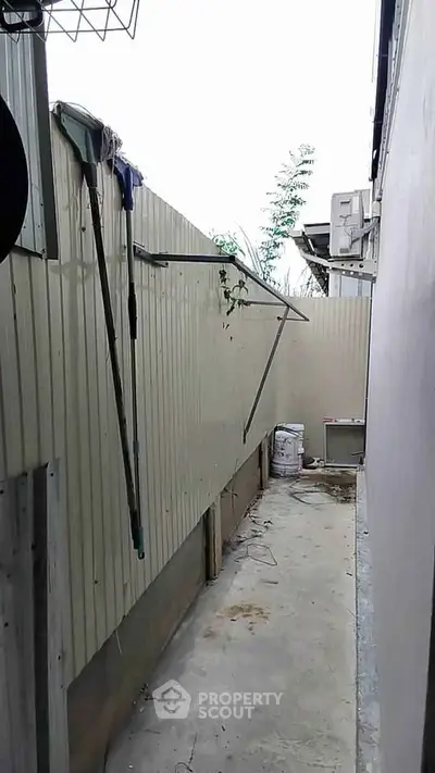Narrow outdoor alley with concrete floor and high fence, ideal for storage or utility use.