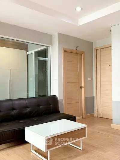 Modern living room with sleek black sofa and stylish coffee table, featuring wooden doors and bright natural lighting.