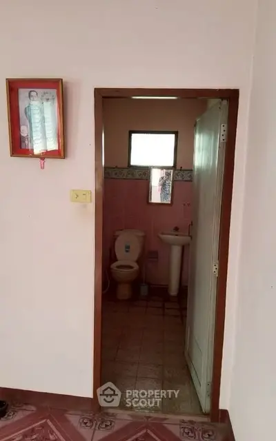 Cozy bathroom with pink tiles and a simple layout, featuring a toilet and sink.