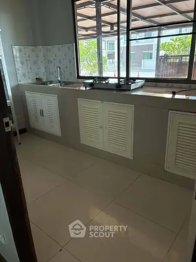 Spacious kitchen with large window and modern cabinetry in a bright home.
