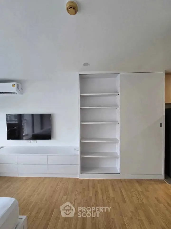 Modern living room with built-in shelves and sleek TV setup, featuring minimalist design and wooden flooring.