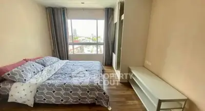 Spacious bedroom with large window and modern furnishings in urban apartment.