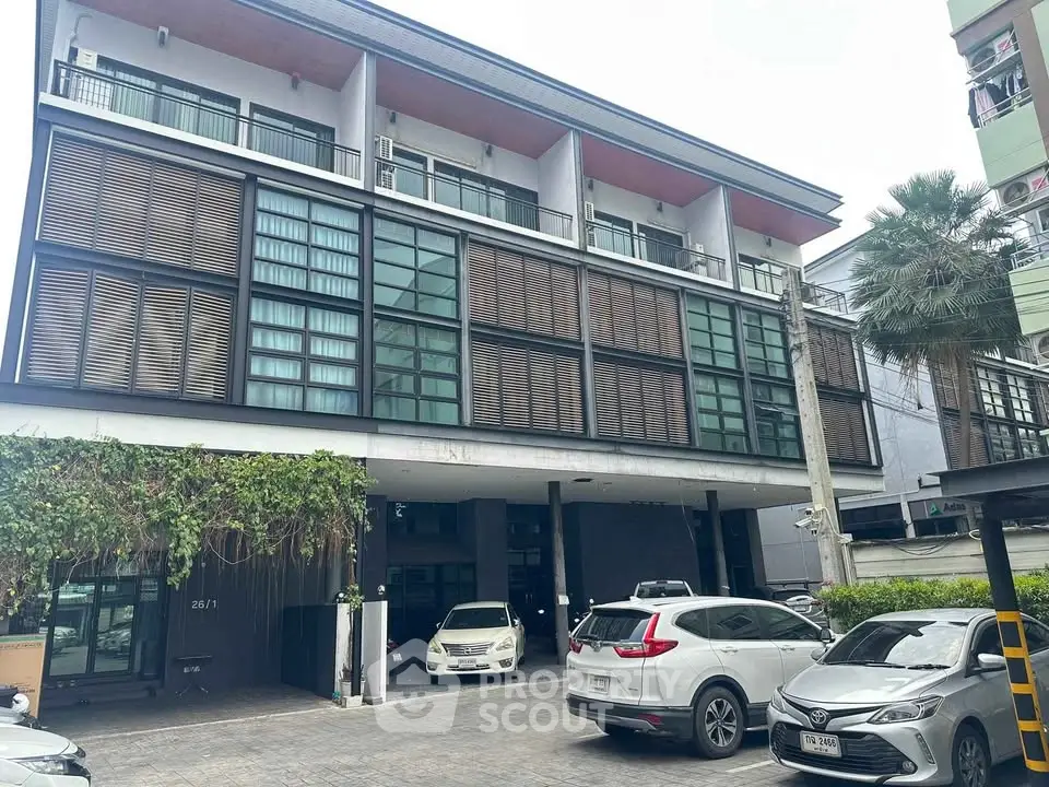 Modern multi-story building with parking area and lush greenery, ideal for urban living or commercial use.